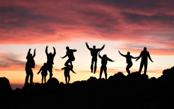 the silhouette of nine people jumping into the air at sunset